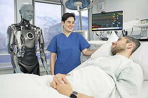 Bild zeigt Person in Krankenhaus-Bett, daneben Pflegeperson und ein humanoider Roboter