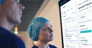 Ärztin und Arzt in OP-Bekleidung vor Screen mit Gesundheitsdaten-Anzeige