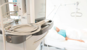 Kabel und Monitor am Krankenhausbett mit Patient im Hintergrund