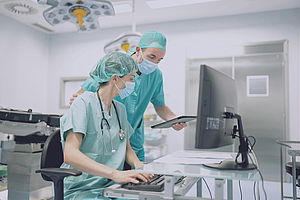 Krankenhauspersonal in der Chirurgie vor Computer mit Laptop in der Hand