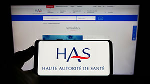 Person holding cellphone with logo of health authority Haute Autorite de Sante (HAS) on screen in front of webpage. Focus on phone display.
