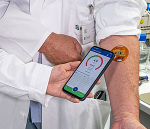 Arzt hält Handy mit geöffneter App an Chip-Pflaster am Arm des Patienten