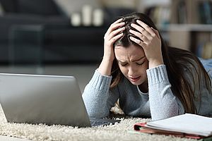 Frau mit verzweifeltem Gesicht und Händen am Kopf vor Laptop