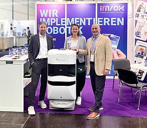 (v.l.) Martin Daller, Elena Bölle (beide imrox) und Marc Avallone (Aethon) mit einem T3-Roboter, am Stand von imrox auf der med.Logistica 2025 in Leipzig